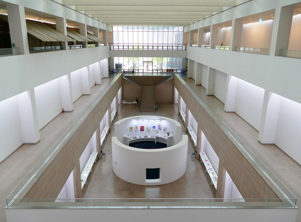 a very symetrically composed photo of a white two storey gallery with a round semi-enclosed room in the centre of the first floor