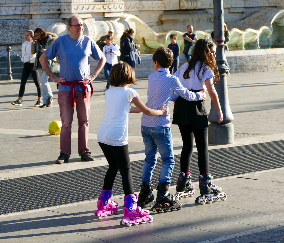three kids in a row linked to each other and gliding along on rollerblades