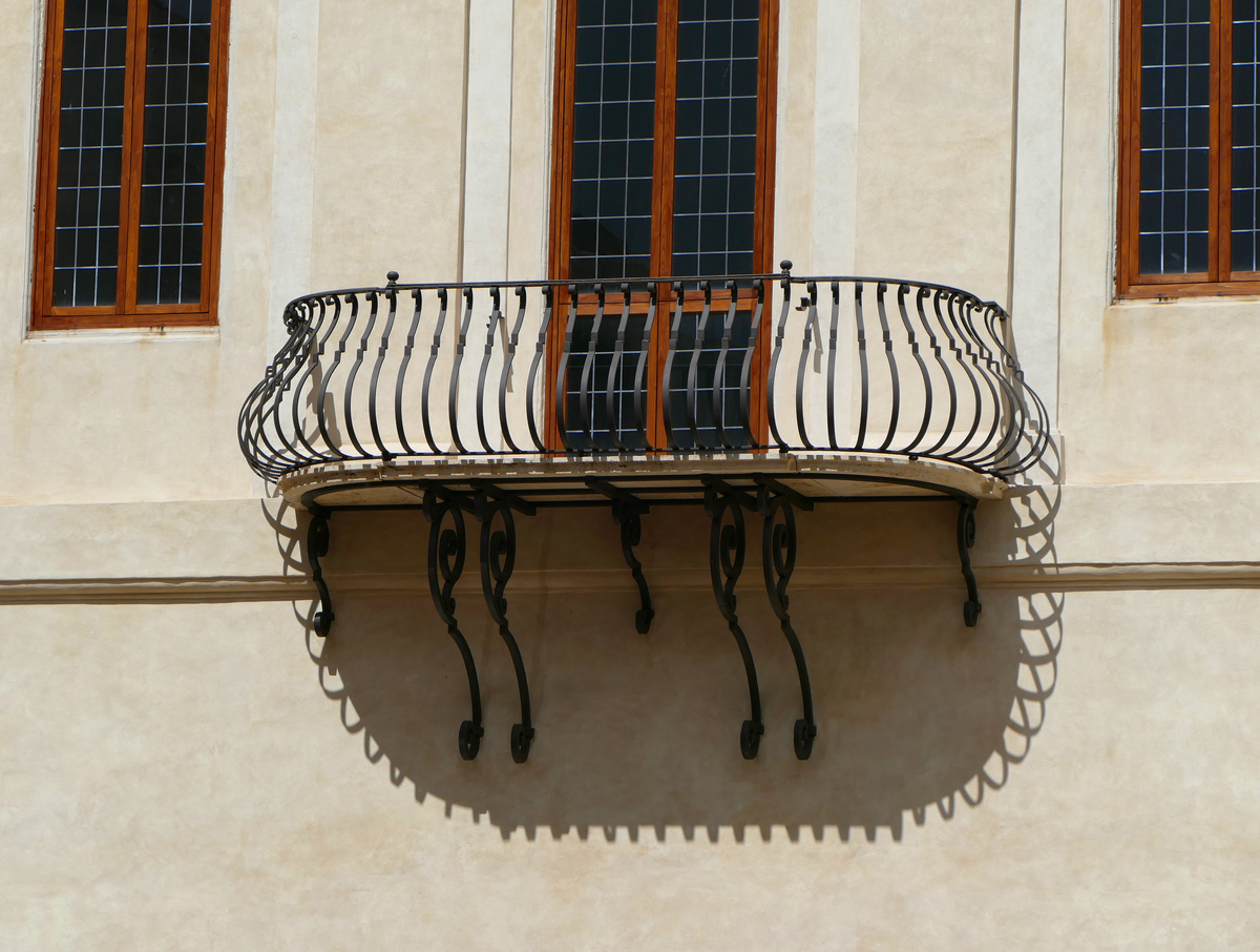 a curving metal-framed balcony casts a shadow on a cream yellow wall