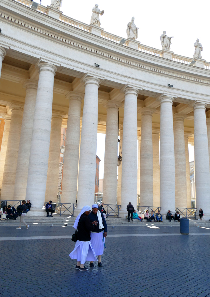 two nuns checking a cellphone as they stand before the columns of St. Peter's Square