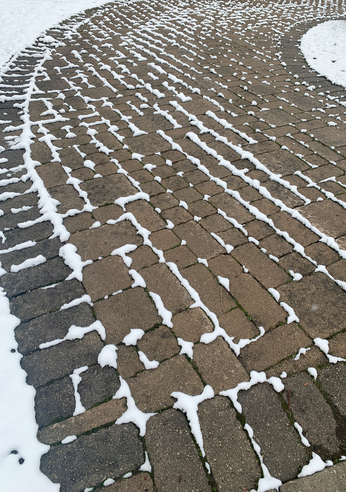 a curving brick driveway with the joints outlined in snow